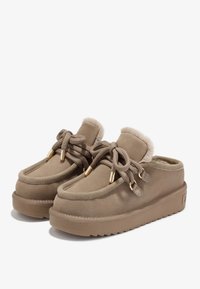 Une paire de chaussons en daim beige de style moccasin avec des semelles épaisses, des dessus à lacets et un pelage en fourrure douce visible autour du col de la cheville.
