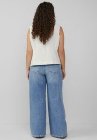 Weißes geripptes ärmelloses Oberteil, kombiniert mit lockeren hellblauen Jeans im weitem Schnitt, die über Taschen auf der Rückseite und einen entspannten Sitz verfügen.