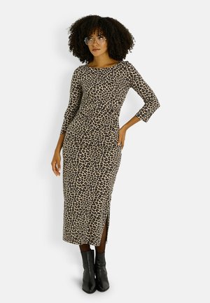 Vestido largo de estampado de leopardo en beige y marrón, con mangas tres cuartos, abertura lateral y silueta ajustada. Combinado con botas negras hasta el tobillo.