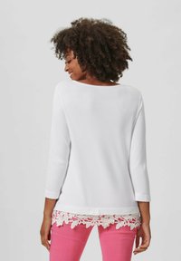 Wit langemouwtop met een ronde halslijn en een bloemenkantafwerking aan de onderkant, gecombineerd met roze broeken. Stel je een gladde textuur en een casual ontwerp voor.