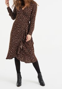 Brun mönstrad omlotterklänning med långa ärmar, volangkant och v-ringning, tillsammans med svarta ankelstövlar och täckande svarta strumpbyxor.