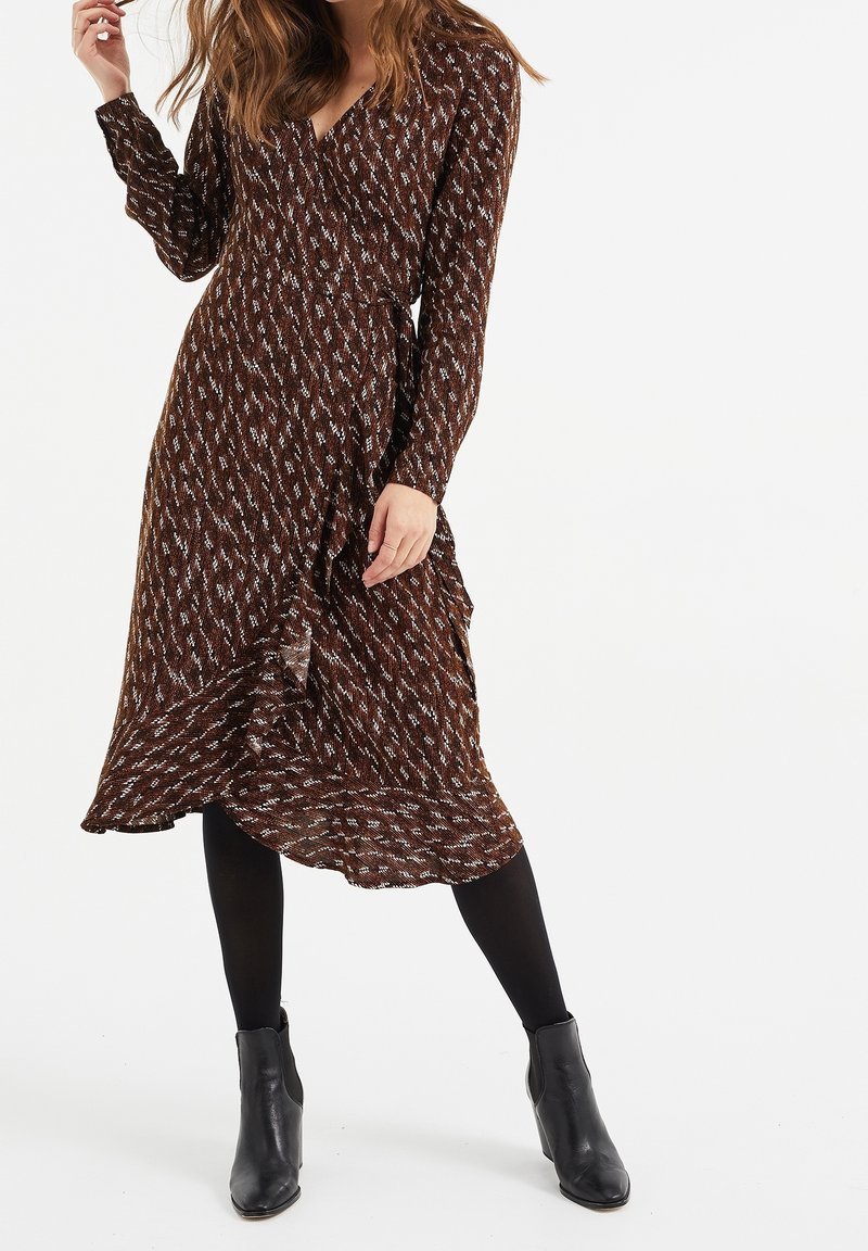 Brun mönstrad omlotterklänning med långa ärmar, volangkant och v-ringning, tillsammans med svarta ankelstövlar och täckande svarta strumpbyxor.
