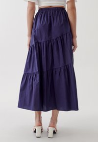 Gonna maxi a strati blu navy realizzata in tessuto morbido, con cintura elastica e una leggera lucentezza, abbinata a mule bianchi con tacco.