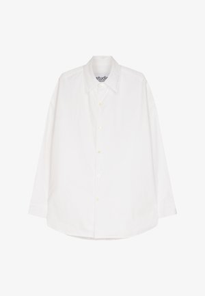 Chemise blanche à manches longues avec un devant boutonné, col standard et une texture lisse semblable au coton. portée avec un pantalon bleu marine.