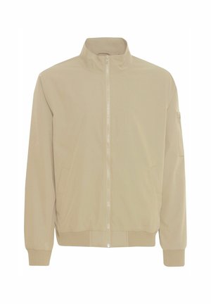 Beige Bomberjacke mit hohem Kragen, seitlichen Taschen, gerippten Bündchen und Saum. Glattes Material und Frontreißverschluss. Detail mit Tasche am linken Arm.
