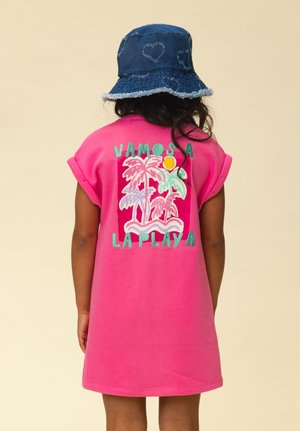 Kind draagt een felroze jurk met palmboomontwerp en de tekst "Vamos a la Playa" op de achterkant, en een blauwe spijkerhoed met hartjespatroon.