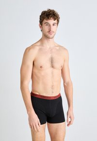 Fekete boxeralsó piros "BJÖRN BORG" derékrésszel. A szabás szoros, anyaga sima és rugalmasnak tűnik. A modellen nincs póló.