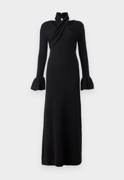 Lång svart klänning i mjukt tyg, med en omslagsliknande midja, hög krage och utsvängda ärmar. Sleek, figurnära silhuett som når golvet.