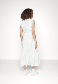 Vit bomulls-midi klänning med broderade detaljer, fransiga ärmar, figursydd midja och lager av volanger nertill, bärs med vita sneakers.