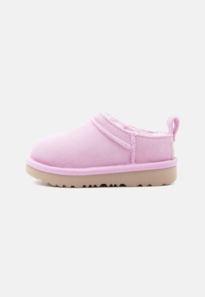 Zapatilla sin cordones de gamuza rosa suave con forro acolchado y suela de goma beige, con una lengüeta en el talón para facilitar su colocación.