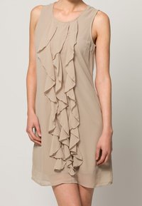 Beżowa sukienka bez rękawów z pionowym wzorem falban, wykonana z lekkiego materiału o gładkiej fakturze.