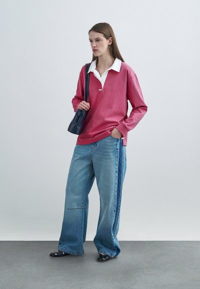 Ροζ πόλο μπλούζα με μακριά μανίκια και λευκό γιακά, συνδυασμένη με μπλε τζιν παντελόνι φαρδιάς γραμμής με ρίγες στα πλάγια και μαύρα μυτερά παπούτσια. Μαύρη τσάντα.