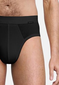 Zwarte katoenen slip met een gladde tailleband, voorzien van een label aan de voorkant. Eenvoudig ontwerp met een goede pasvorm, met vlakke naden en minimale detailing.