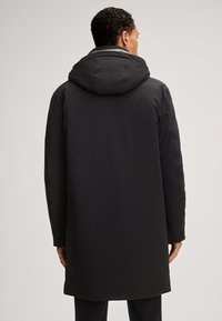 Czarna wodoodporna parka z kapturem, długimi rękawami i prostym krojem. Gładka tekstura, minimalistyczny design, bez widocznych elementów metalowych lub akcentów.