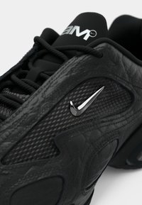 Μαύρο αθλητικό παπούτσι με υφή που συνδυάζει λείο δέρμα και δίχτυ. Διακριτικό ασημί λογότυπο Nike swoosh στο πλάι.