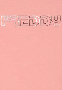 Camiseta de algodón rosa con un gran gráfico metálico plateado que dice "FREDDY" en la parte delantera, con una tipografía moderna y audaz.