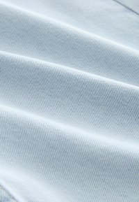 Ljusblå denimtextil med en slät yta och diagonala ribbor. Har subtil sömnad längs kanterna, vilket ger en klassisk avslappnad look.