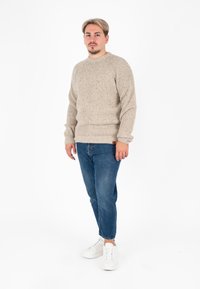 Beżowy sweter dziergany z prążkowanym teksturem, okrągłym dekoltem i długimi rękawami, w połączeniu z niebieskimi dżinsami i białymi trampkami. Wygodny krój.