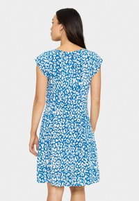 Robe bleue avec un design à manches courtes, recouverte d'un motif abstrait blanc. Jupe évasée avec une texture subtile et un détail au niveau du dos.