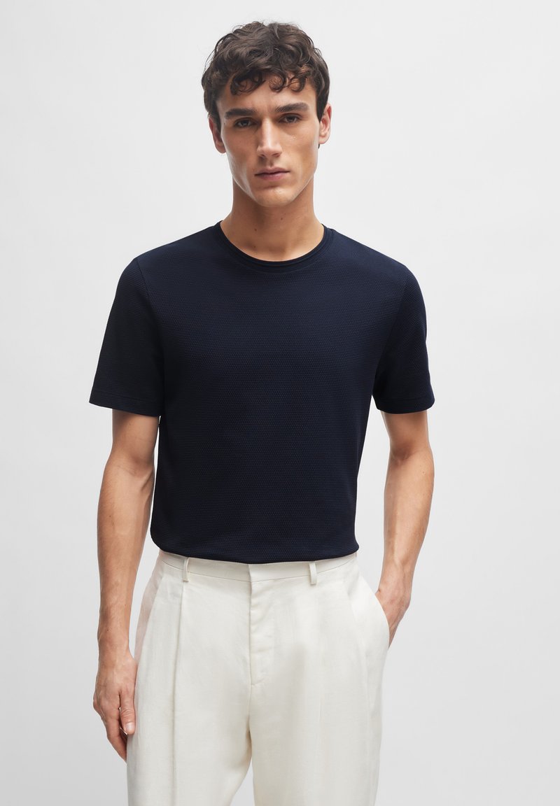 Marineblå kortærmet t-shirt i tekstureret stof med rund halsudskæring, parret med lysfarvede, skræddersyede bukser. Minimalistisk design.