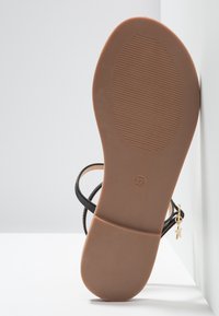 Mustassa narusandaalissa on teksturoitu ruskea pohja, jossa on tähti-riipus ja koko 37 painettuna. Silkkisissä naruissa on minimalistinen muotoilu.