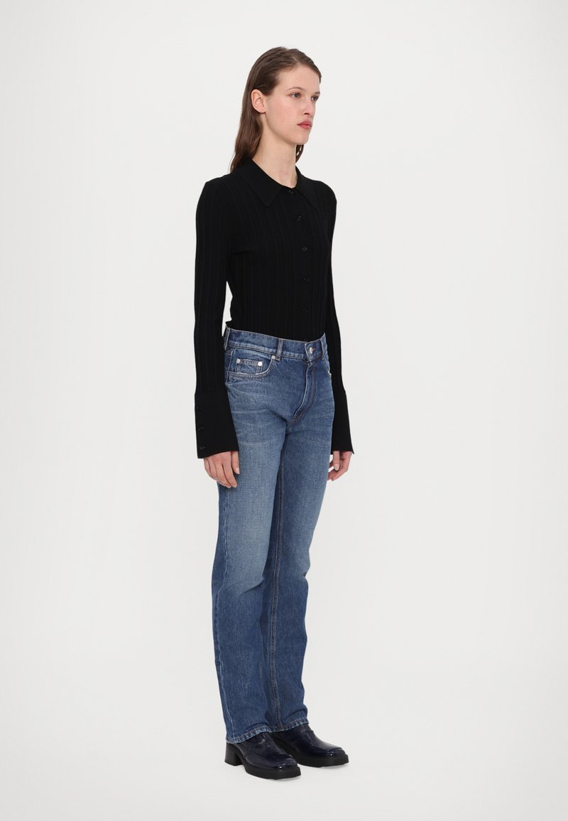 Chemise noire à rayures, à manches longues et à boutons, avec un col, associée à un jean bleu clair à jambe droite et des bottines noires brillantes.