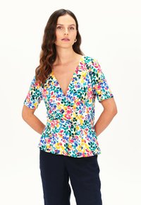 Top con estampado floral y escote en V profundo, mangas cortas y dobladillo peplum. Presenta colores vibrantes sobre un fondo blanco. Textura de tela suave.