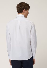 Chemise blanche à manches longues, en coton, coupe régulière, col pointu, détail au dos, poignets avec boutons, texture lisse, design simple.
