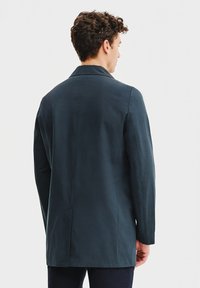 Ciemnoniebieska marynarka o dopasowanym kroju, z kołnierzem w szpic i gładką fakturą. Minimalistyczny design bez widocznych elementów metalowych ani ozdób.