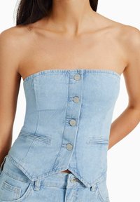 Ljusblå denimkorset med en axelbandslös design, som har fem knappar framtill och två sidofickor. Slät textur med en skräddarsydd passform.