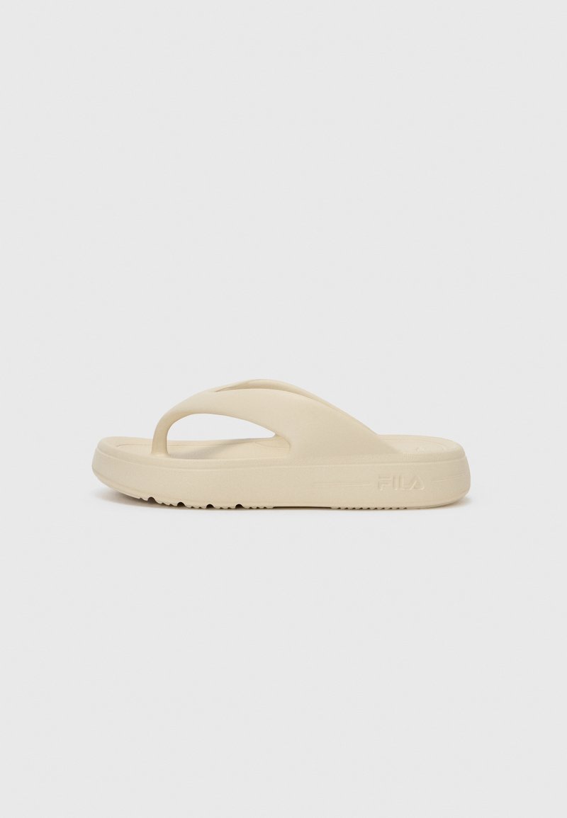 Beige flip-flop sandaali, joka on valmistettu kumista, ja siinä on yksi varvasnauha ja paksu pohja, jossa on kuvioitu pito. Merkitty Fila-logolla.