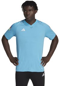 Lichtblauw sportshirt met een V-hals, textuurstof en subtiele ventilatiegaten. Bevat het witte Adidas-logo en kleurrijke accenten op de schouders.
