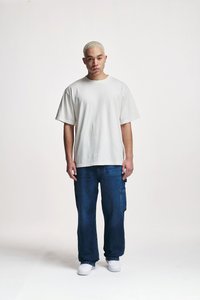 Svijetlosivi preveliki T-shirt s kratkim rukavima, uparen s tamnoplavim trapericama s džepovima. Model nosi bijele tenisice.