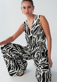 Zwart-wit zebraprint jumpsuit met een diepe V-hals, wijde pijpen en een strikdetail in de taille, gemaakt van lichtgewicht stof.
