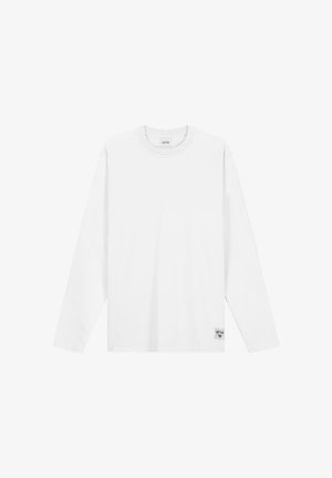 Maglietta bianca a maniche lunghe con scollo rotondo, con etichetta vicino all'orlo e targhetta del marchio all'interno del collo, su sfondo bianco uniforme.