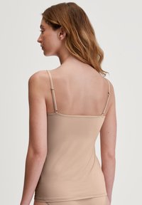 Aansluitende naadloze nude cami met verstelbare dunne bandjes, gemaakt van een zachte stof, met een eenvoudig ontwerp en een naadloze achterkant.