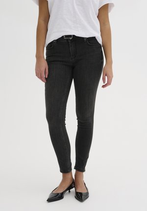Black skinny jeans made of denim, featuring a mid-rise waist, five pockets, and subtle stitching details. Paired with black pointed-toe shoes.