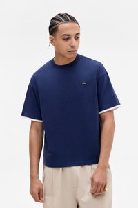 Marineblå bomuld T-shirt med korte ærmer, hvid kant og lille logo på venstre bryst. Løst fit og blød tekstur.