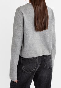 Gray wool sweater with a round neckline, slightly cropped length, and long sleeves, paired with dark jeans featuring rear pockets.