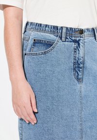 Vaaleansininen farkuhame, jossa on elastinen vyötärö, etutasku ja kontrastivärinen ompelu. Sileä pinta ja suora leikkaus.