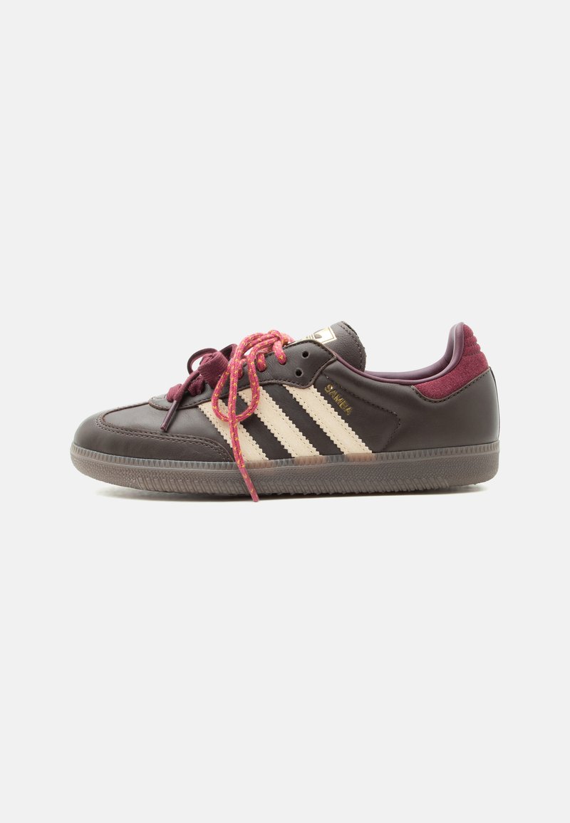 Σκούρο καφέ αθλητικό παπούτσι Adidas Samba με κρεμ ρίγες, μπορντό τακούνι και ροζ κορδόνια με σχέδιο, εμφανισμένο σε προφίλ στο λευκό φόντο.