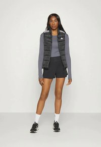 Juodas pūkinis liemenė su horizontaliais siūlės ant pilkos ilgomis rankovėmis maikės, derinama su juodomis šortais ir juodais sportiniais batais.