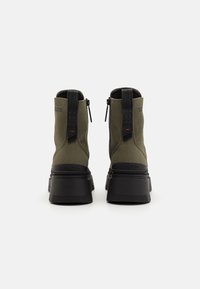 Botas de tobillo de lienzo verde con suelas de goma negra y cremalleras laterales, con un talón texturizado y un detalle de logo embosado en la parte trasera.