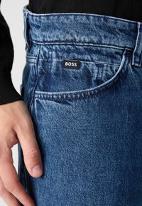 Vaqueros de mezclilla azul con un acabado desgastado, que presentan una etiqueta negra "BOSS" en la cintura y un clásico diseño de cinco bolsillos.