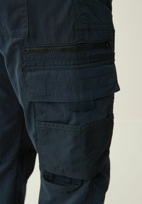 Temno modri cargo hlače z več žepi, z zip žepom z črnimi dodatki in teksturirano tkanino za vzdržljivost.