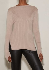 Ljusbeige ribbad tröja med lång ärm och sidofickor. Har en vid halsringning och diagonala ribbmönster på framsidan.