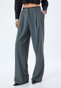 Graue hochtaillierte weite Hosen aus strukturiertem Stoff, mit Vorderfalten und Seitentaschen, kombiniert mit spitzen schwarzen Schuhen.