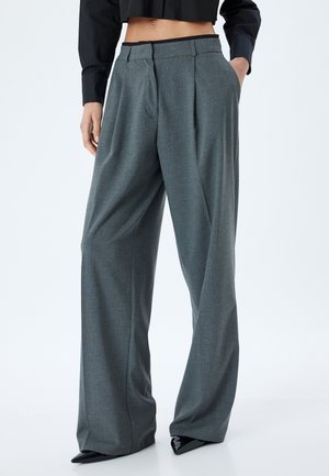 Grijze hoge taille wijde broek gemaakt van textuurstof, met voorplooien en zijzakken, gestyled met puntige zwarte schoenen.