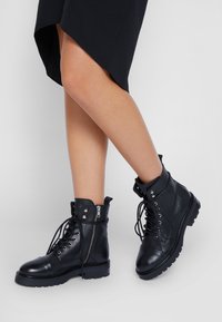 Bottines en cuir noir avec un design à lacets, fermeture éclair sur le côté, accents métalliques et semelles épaisses texturées, dotées d'un bout arrondi.
