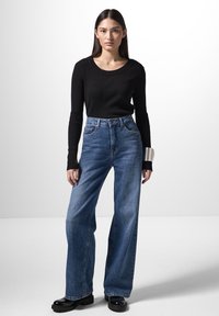 Top lungo a maniche lunghe a coste nere, jeans larghi a vita alta blu e scarpe con piattaforma nere. Texture morbide, design informale e silhouette strutturata.
